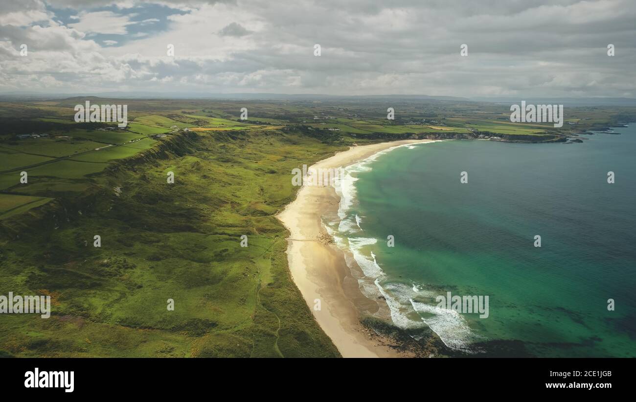 White Beach sabbia costa zoom aereo, Antrim County, Nortern Irlanda. Paesaggio epico di verde scogliera costa della baia oceano Atlantico. Acqua calma al tramonto nuvoloso giorno. Foto Stock