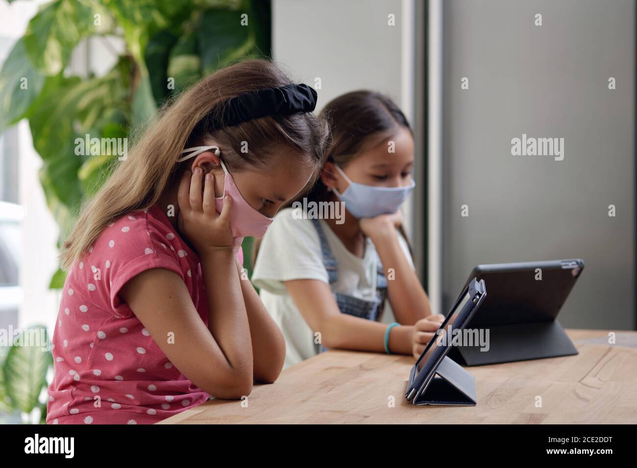 Le studentesse multietniche indossano maschere siedono alla scrivania guardare lo schermo del tablet si sente disturbato pensare a studio attività da remoto. Gadget di generazione Alpha overu Foto Stock