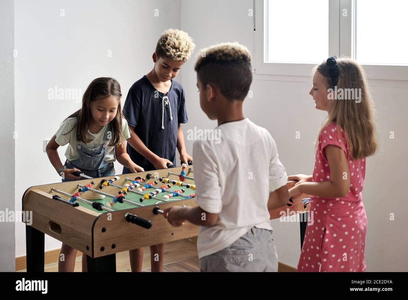 Gruppo di bambini carino multiculturale stand al coperto trascorrere il tempo di gioco con gli amici giocare a foosball insieme. Versione da tavolo degli amanti del calcio. Avendo fu Foto Stock