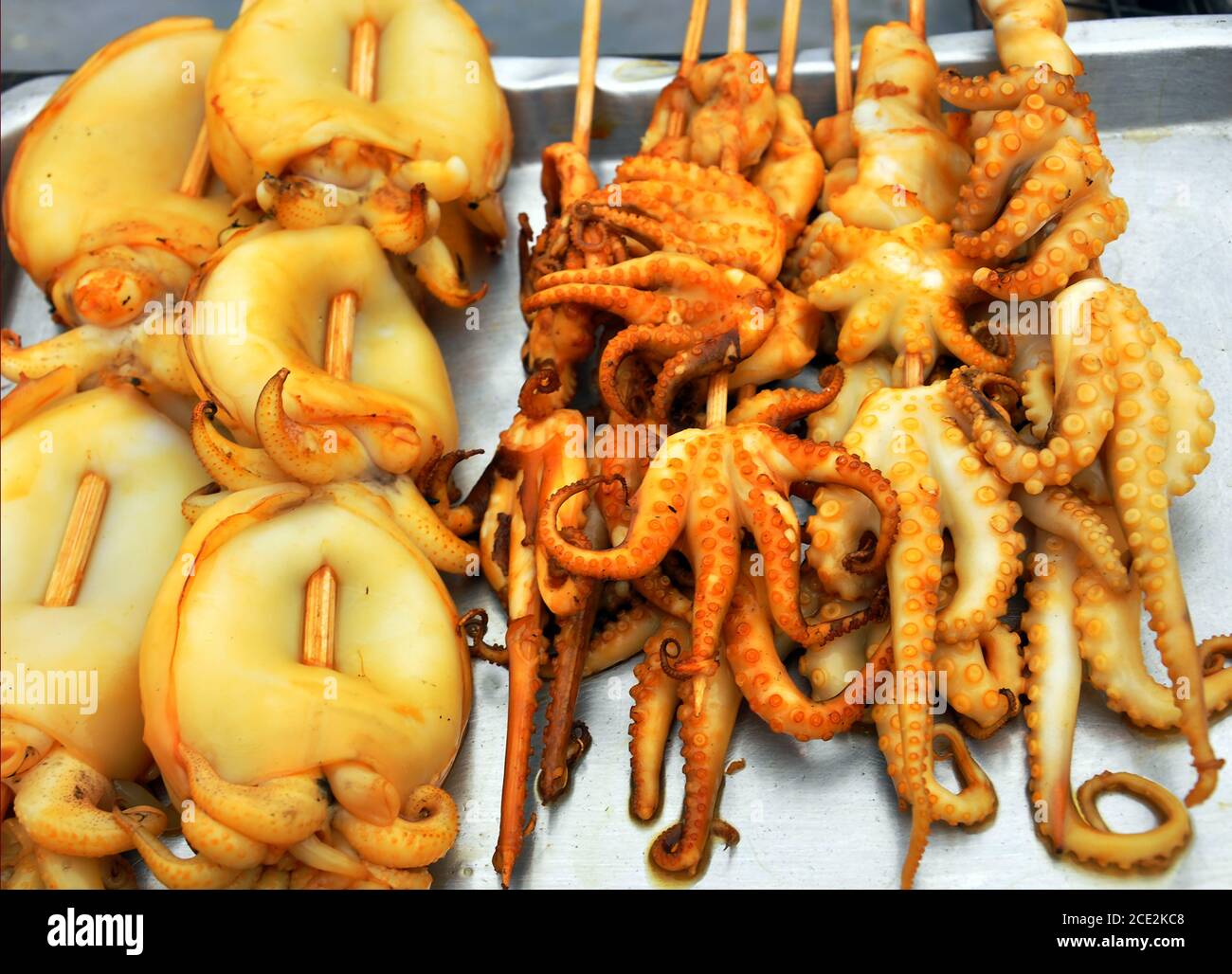 Primo piano di calamari dorati e polpo su spiedini di legno offerti dai venditori di cibo di strada a Bangkok, Thailandia Foto Stock