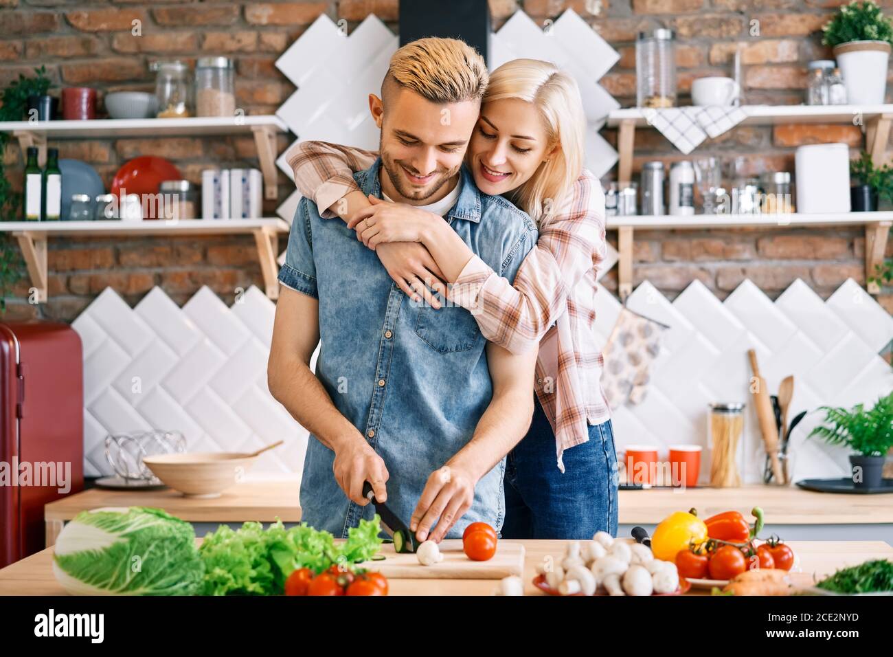 Sorridente giovane coppia che cucina insieme pasto vegetariano in cucina a casa. Donna che abbraccia l'uomo Foto Stock