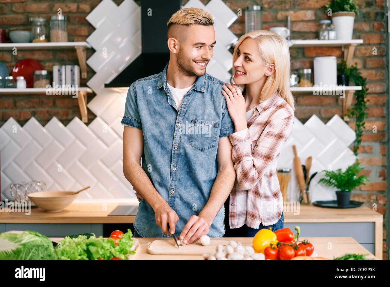 Una giovane coppia sorridente che cucinava insieme un pasto vegetariano in cucina a casa Foto Stock