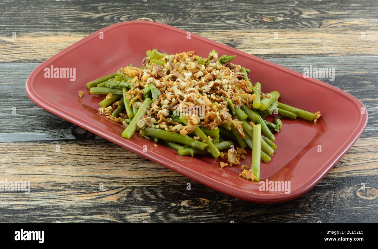 Asparagi tritati con noci pecan e condimenti croccanti piatto di portata rosso Foto Stock