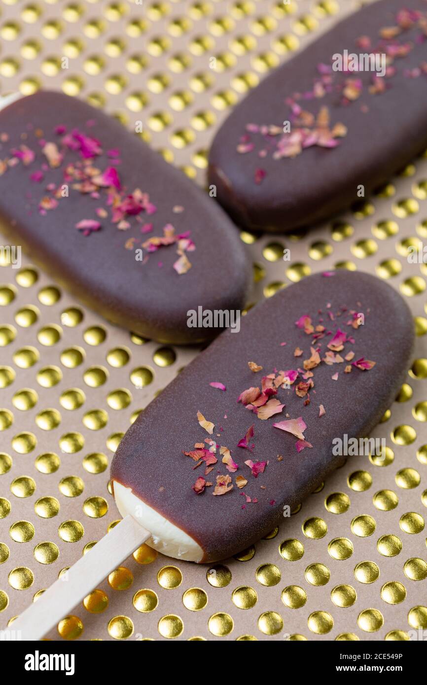 Gelato su un bastone in una glassa di cioccolato fondente con petali di rosa. Foto Stock