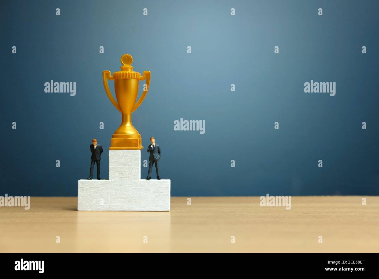 Concetto di business in miniatura - uomo d'affari in piedi davanti al bianco podio vincitore con trofeo d'oro Foto Stock