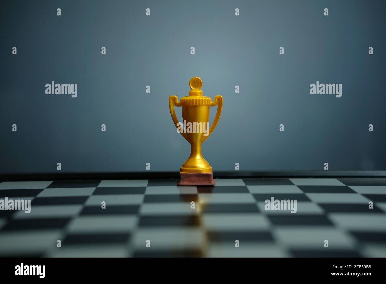 Foto concettuale della strategia aziendale – trofeo d'oro in piedi sulla scacchiera con pedina di scacchi Foto Stock