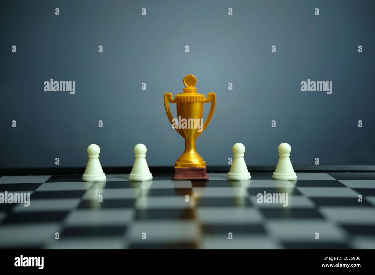 Foto concettuale della strategia aziendale – trofeo d'oro in piedi sulla scacchiera con pedina di scacchi Foto Stock