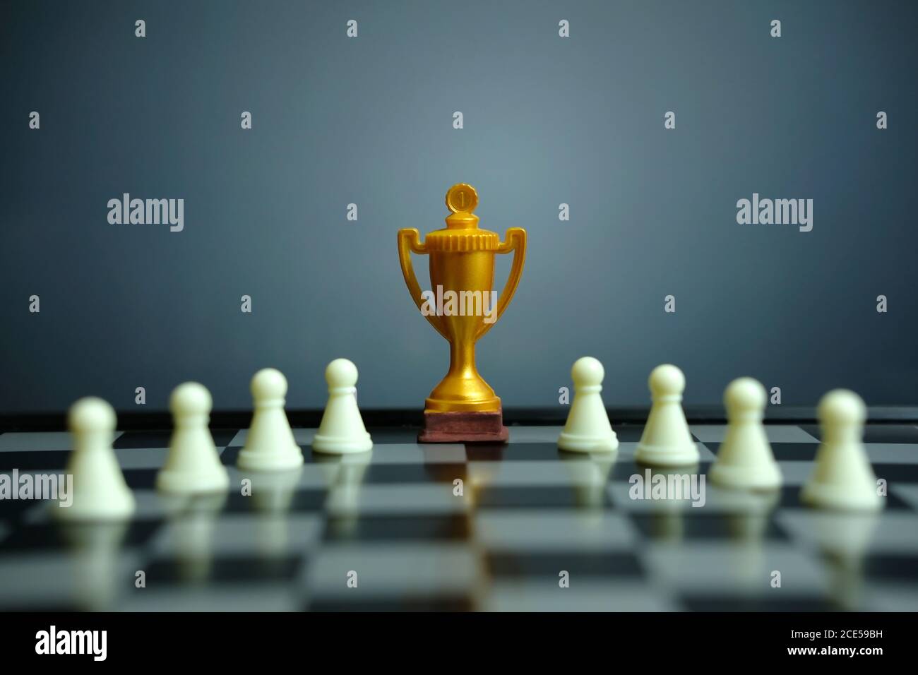 Foto concettuale della strategia aziendale – trofeo d'oro in piedi sulla scacchiera con pedina di scacchi Foto Stock