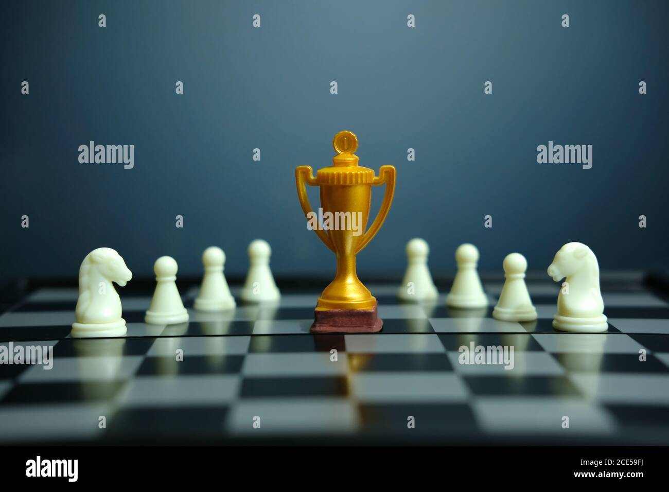 Foto concettuale della strategia aziendale – trofeo d'oro in piedi sulla scacchiera con pedina di scacchi Foto Stock