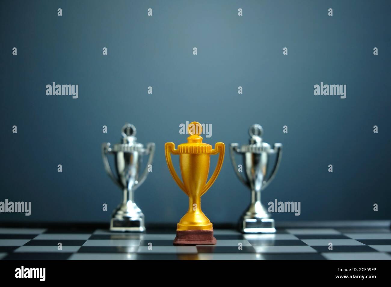 Foto concettuale della strategia aziendale – trofeo d'oro in piedi sulla scacchiera con pedina di scacchi Foto Stock