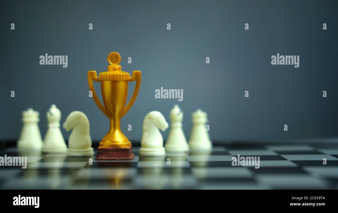 Foto concettuale della strategia aziendale – trofeo d'oro in piedi sulla scacchiera con pedina di scacchi Foto Stock
