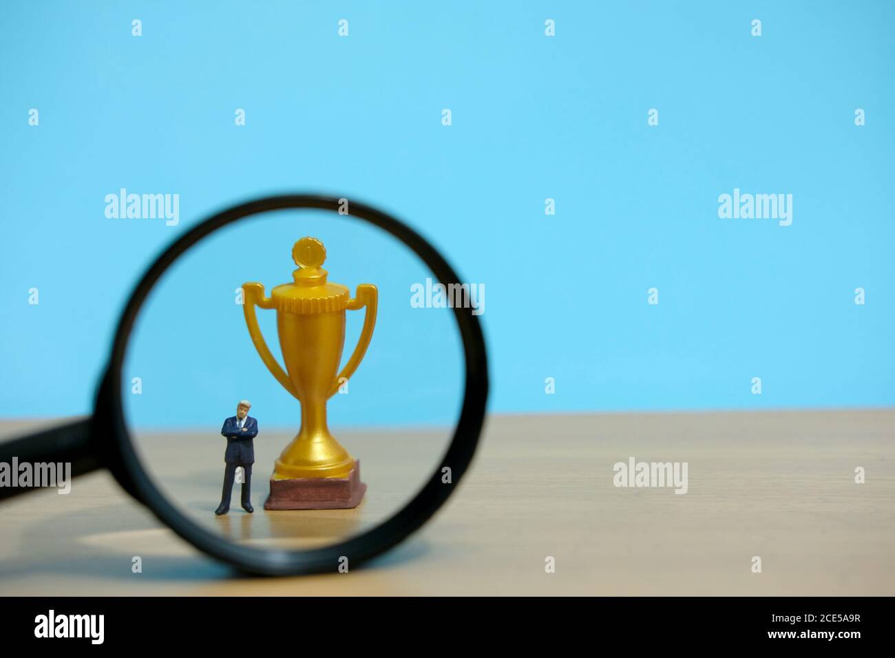 Concetto di business in miniatura - uomo d'affari in piedi di fronte all'oro trofeo e lente d'ingrandimento in vetro Foto Stock