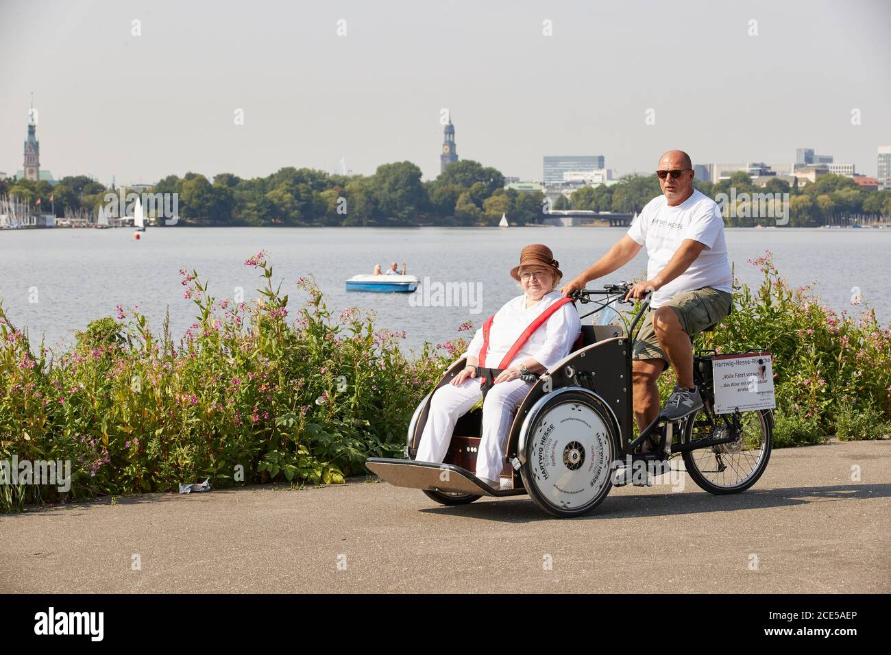 Amburgo, Germania. 14 agosto 2020. Jörg Larisch, un tirocinante di 57 anni, prende Brigitte Polz (77), un residente del complesso residenziale degli anziani 'Hartwig-Hesse-Quartier', in un'escursione al lago di Alster sulla bici da carico 'Hartwig-Hesse-Rickshaw'. Sullo sfondo si può vedere la torre del 'Michel', la chiesa principale di San Michele e il municipio di Amburgo (l). (A dpa ''Best decision'' - 57-year-old fa l'addestramento nella cura geriatrica') accreditamento: Georg Wendt/dpa/Alamy Live News Foto Stock