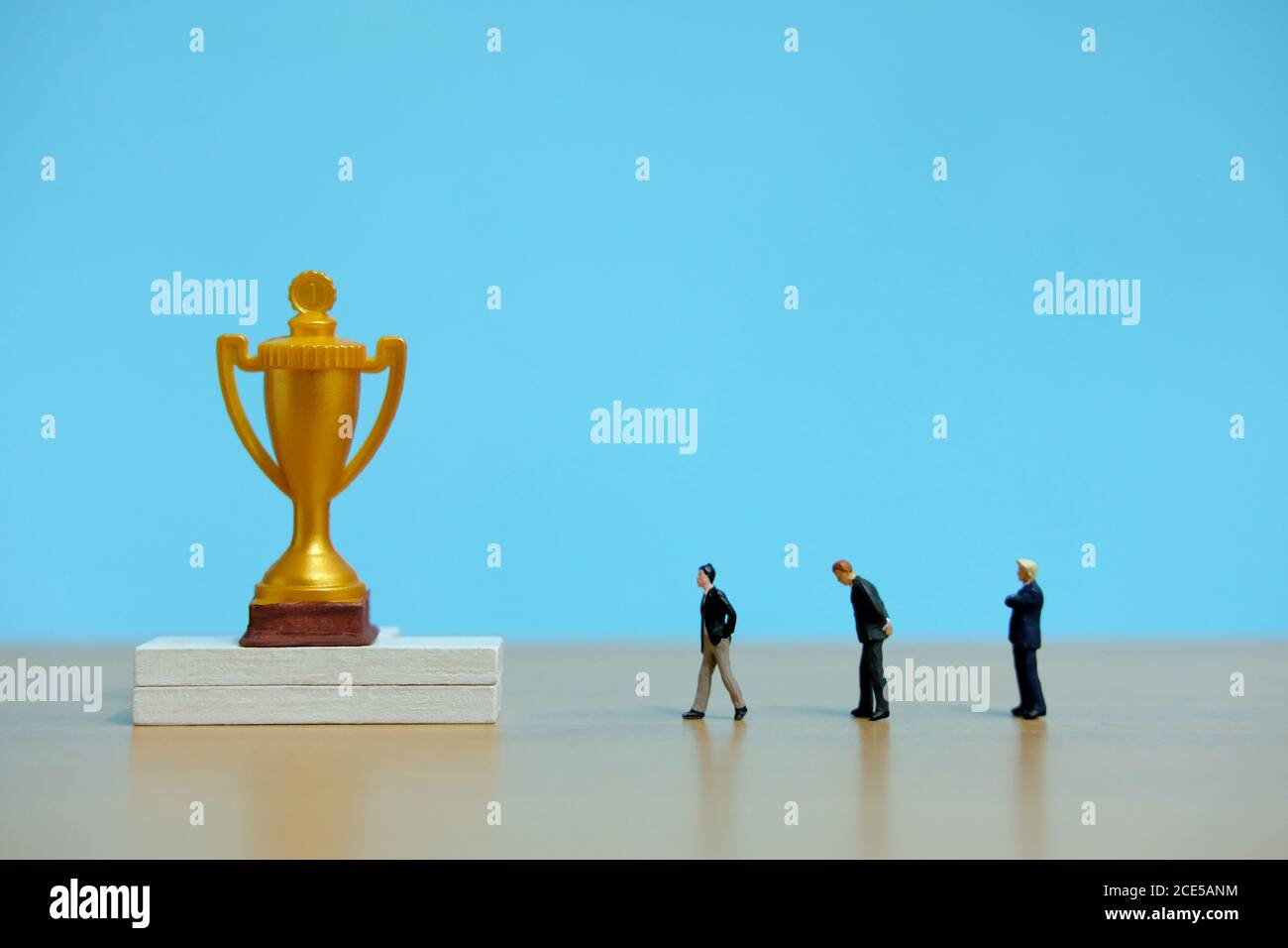 Concetto di business in miniatura - gruppo di uomini d'affari che si allineano dietro il trofeo d'oro Foto Stock