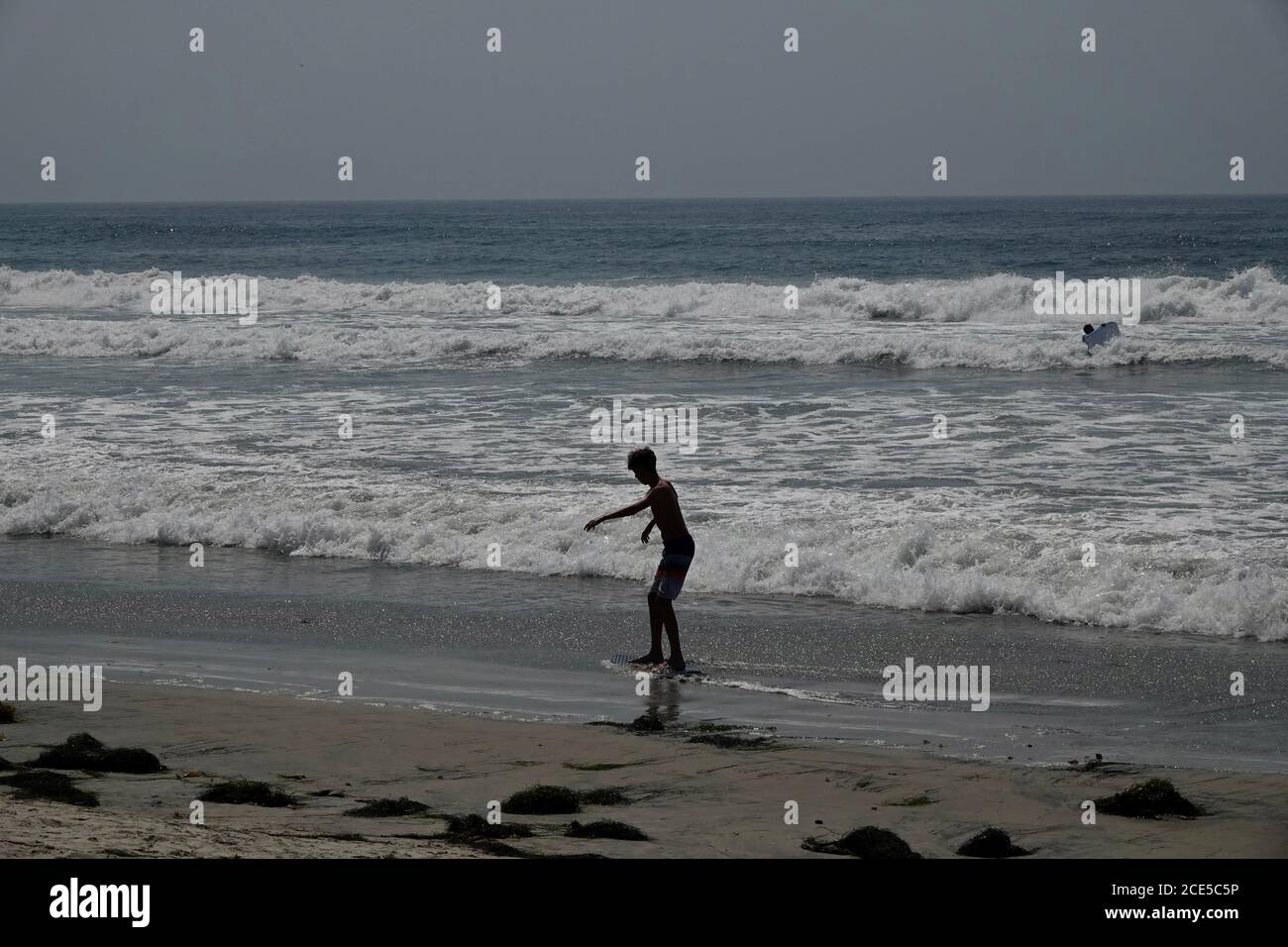 Una silhouette di un ragazzo skim boarding vicino agli oceani bordo sulla spiaggia. Foto Stock