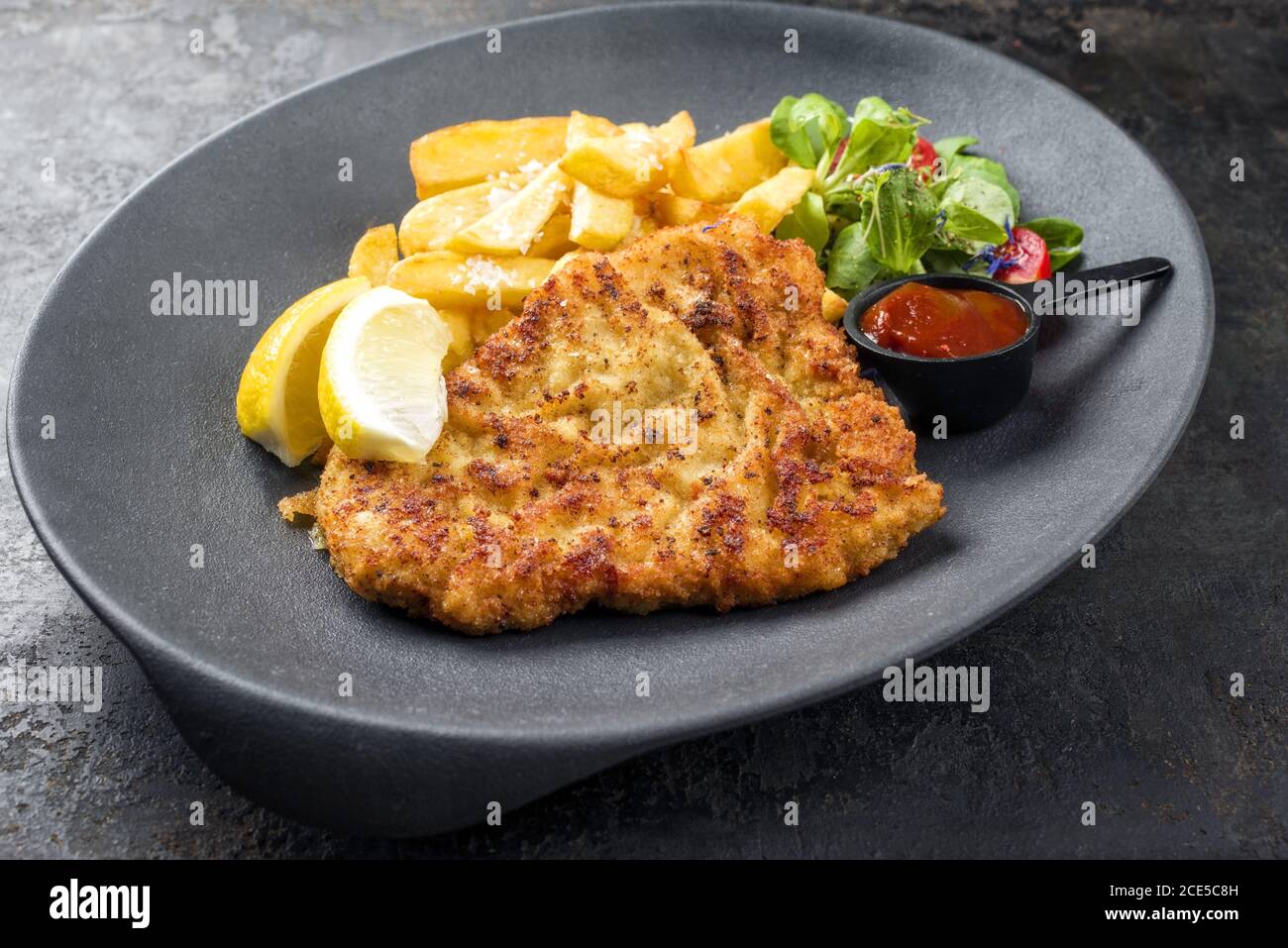 Schnitzel di Wiener fritto dalla parte superiore di vitello con patatine fritte e lattuga come primo piano su una piastra di design moderno Foto Stock