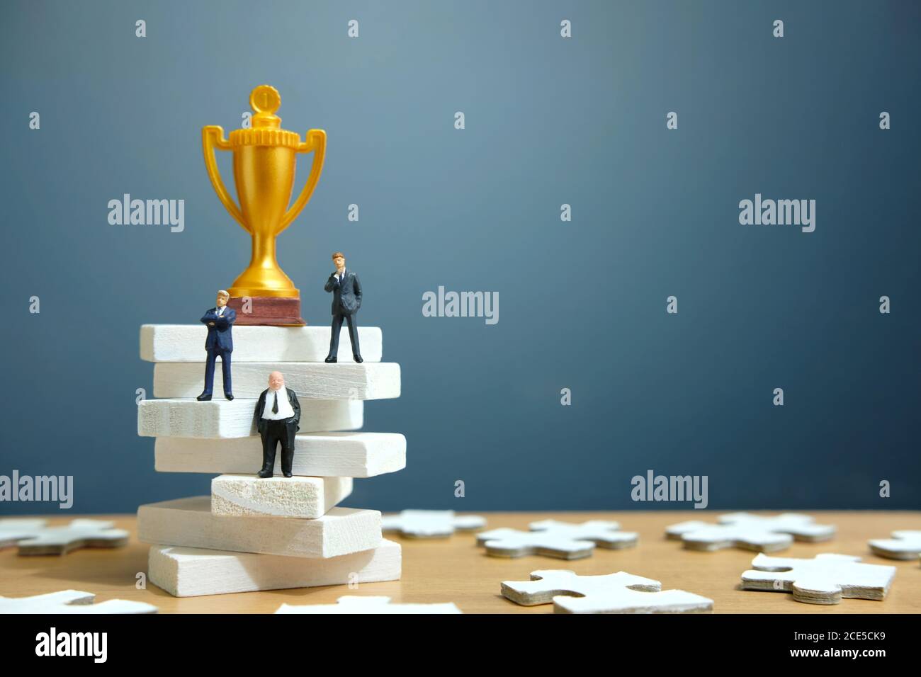 Concetto di business in miniatura - uomo d'affari in piedi su scala scala bianca con trofeo d'oro sopra di esso Foto Stock