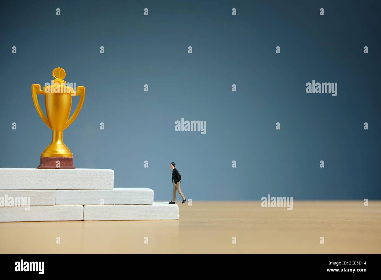 Concetto di business in miniatura - uomo d'affari che cammina sulla scala bianca per raggiungere il trofeo d'oro Foto Stock