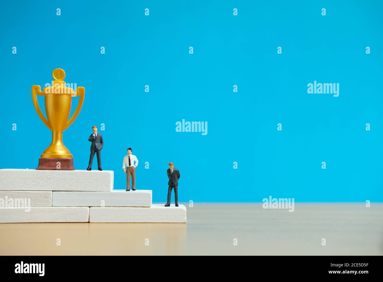 Concetto di business in miniatura - uomo d'affari in piedi sul podio bianco vincitore con trofeo d'oro e d'argento Foto Stock