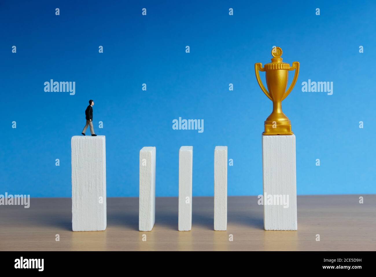 Concetto di affari in miniatura - uomo d'affari che cammina nella parete di ostacolo della scala per raggiungere il trofeo d'oro Foto Stock