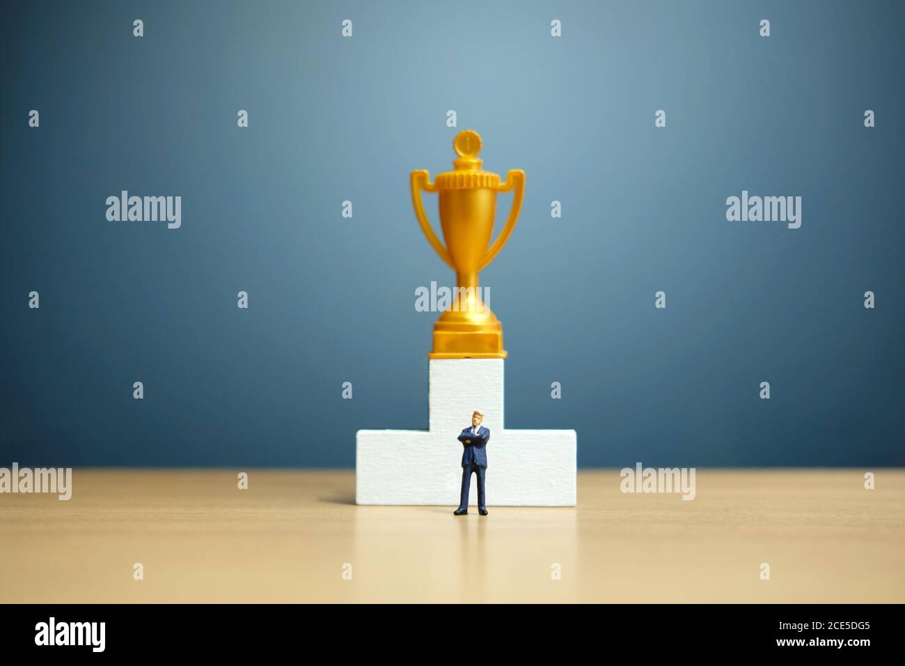 Concetto di business in miniatura - uomo d'affari in piedi davanti al bianco podio vincitore con trofeo d'oro Foto Stock