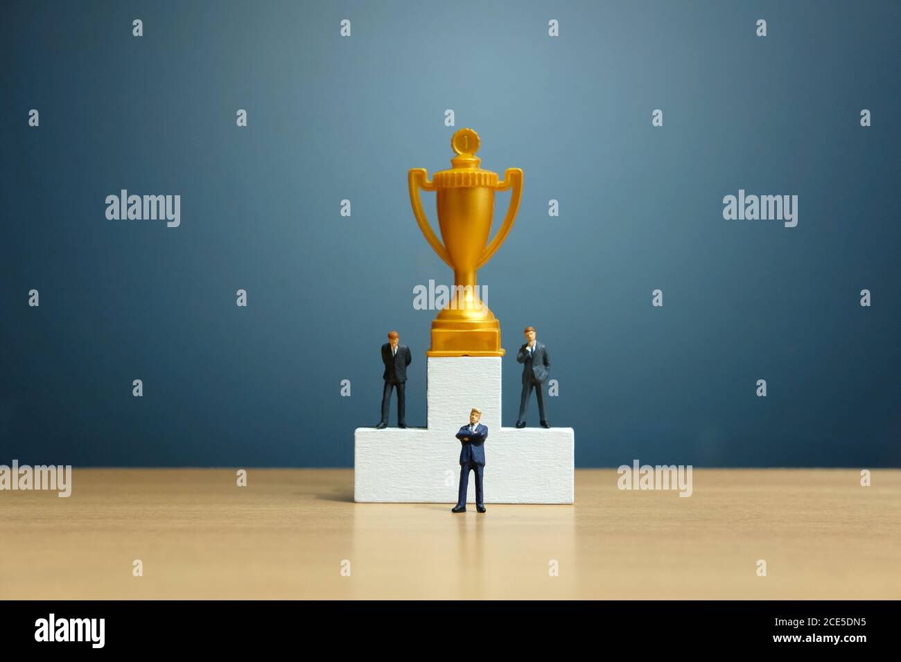 Concetto di business in miniatura - uomo d'affari in piedi davanti al bianco podio vincitore con trofeo d'oro Foto Stock