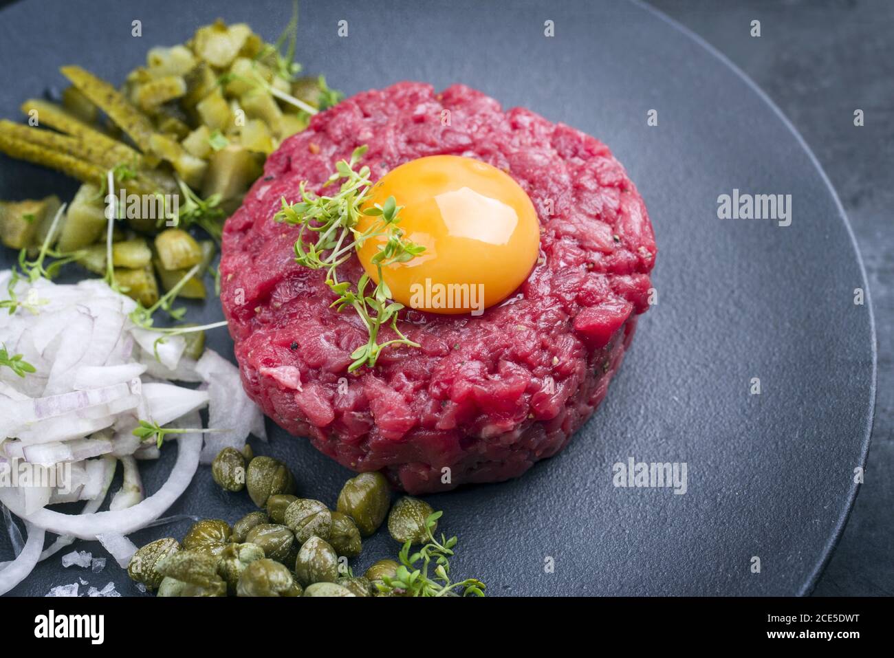 Tartaro gourmet crudo di filetto di manzo con il giallo dell'uovo e del gherkin con capperi e anelli di cipolla come primo piano sul design moderno p Foto Stock