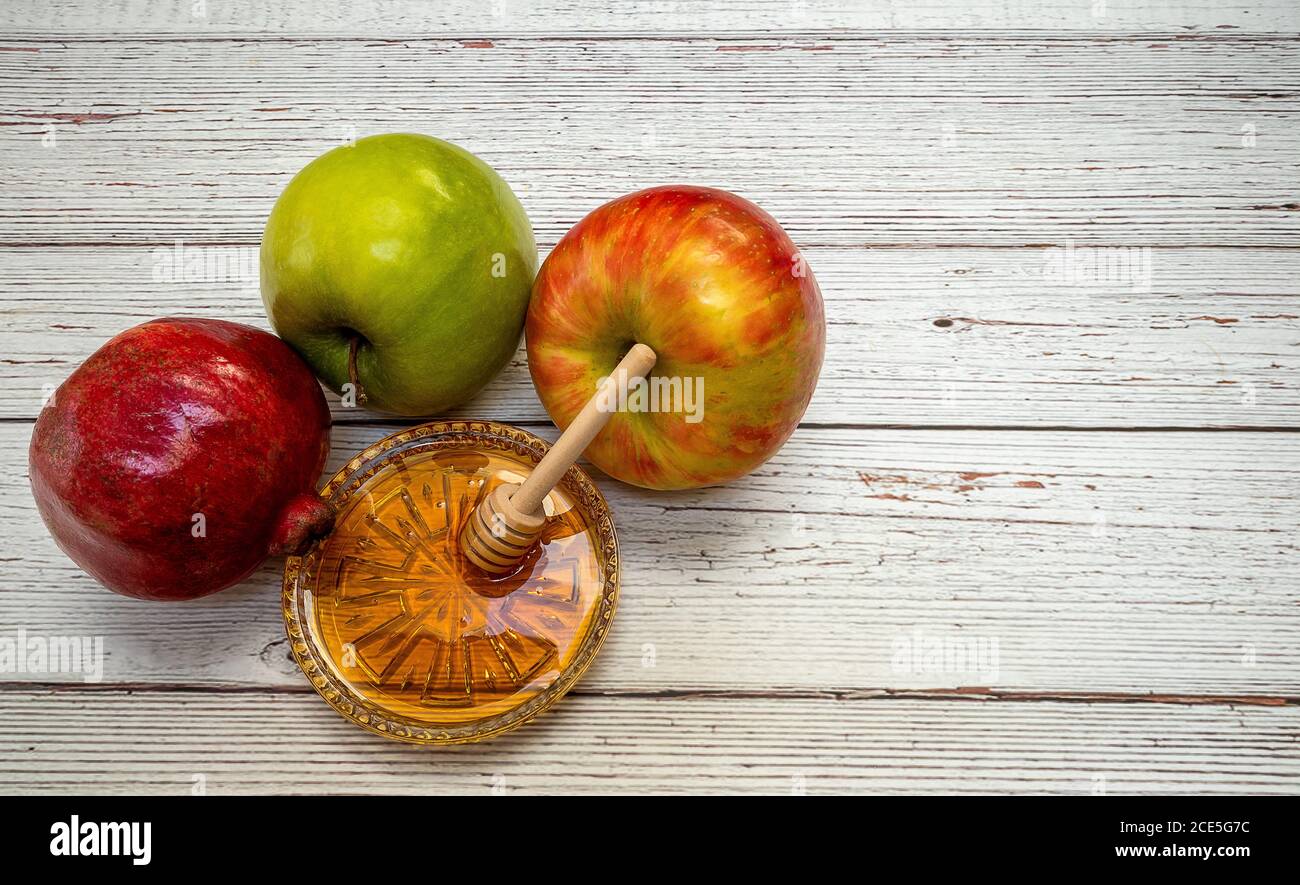 Prodotti tradizionali per la celebrazione del Rosh Hashanah - mele, melograno, miele, favi - su sfondo bianco di legno Foto Stock