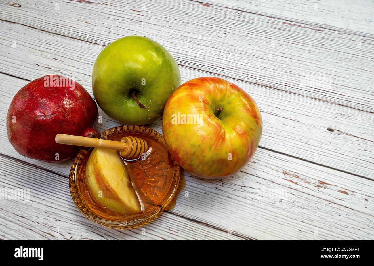 Prodotti tradizionali per la celebrazione del Rosh Hashanah - mele, melograno, miele, favi - su sfondo bianco di legno Foto Stock