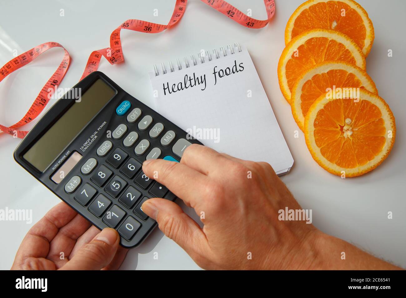 Fette arancioni, una nota vuota con una penna e un nastro di misurazione. Calcolo delle calorie su una calcolatrice. Concetto di dieta Foto Stock