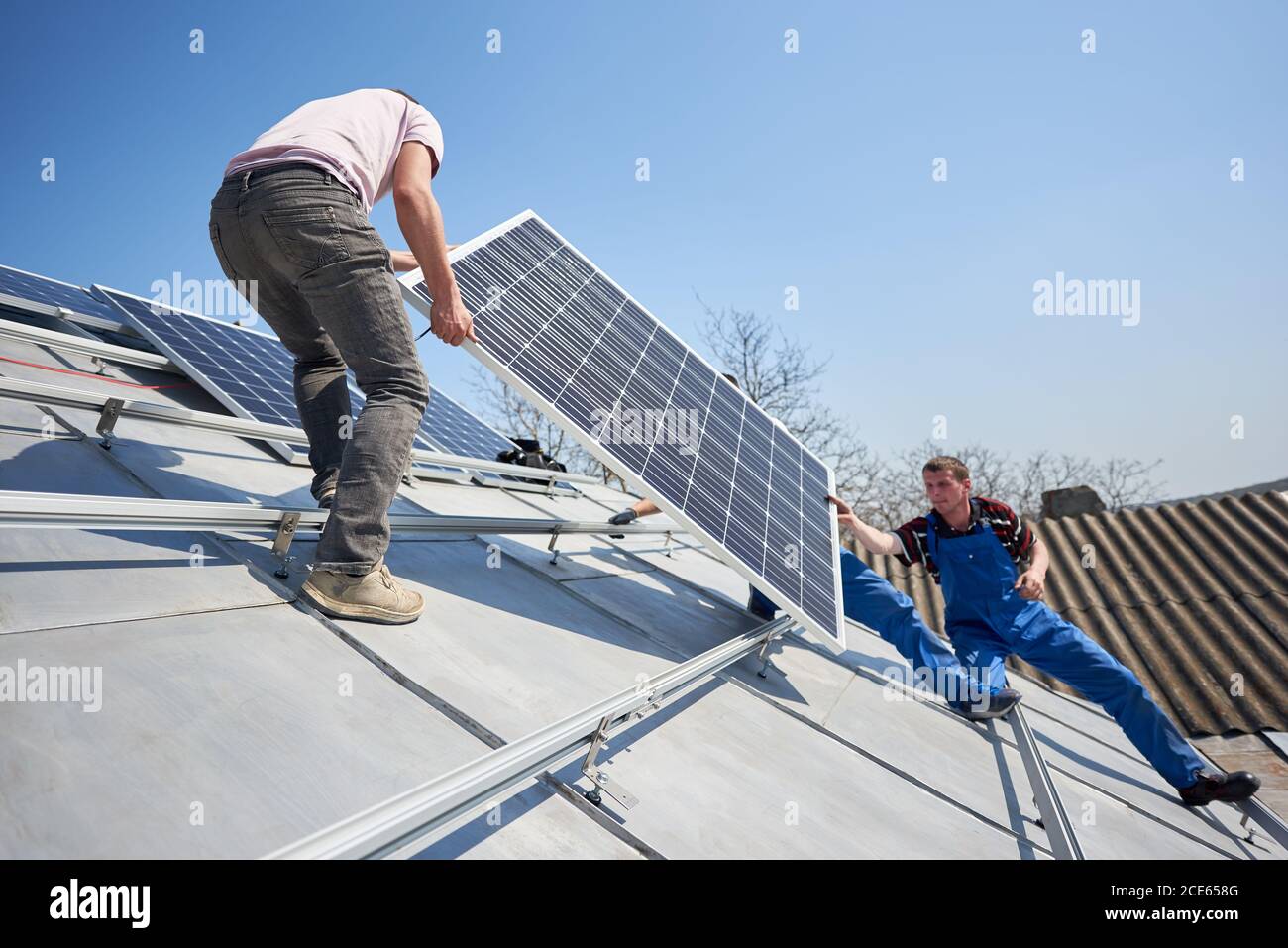 Lavoratori di sesso maschile che installano un sistema autonomo di pannelli fotovoltaici solari. Elettricisti che sollevano il modulo solare blu sul tetto della casa moderna. Foto Stock