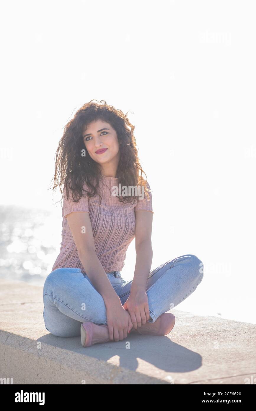 Donna felice sedette sulla spiaggia guardando via sorridente Foto Stock