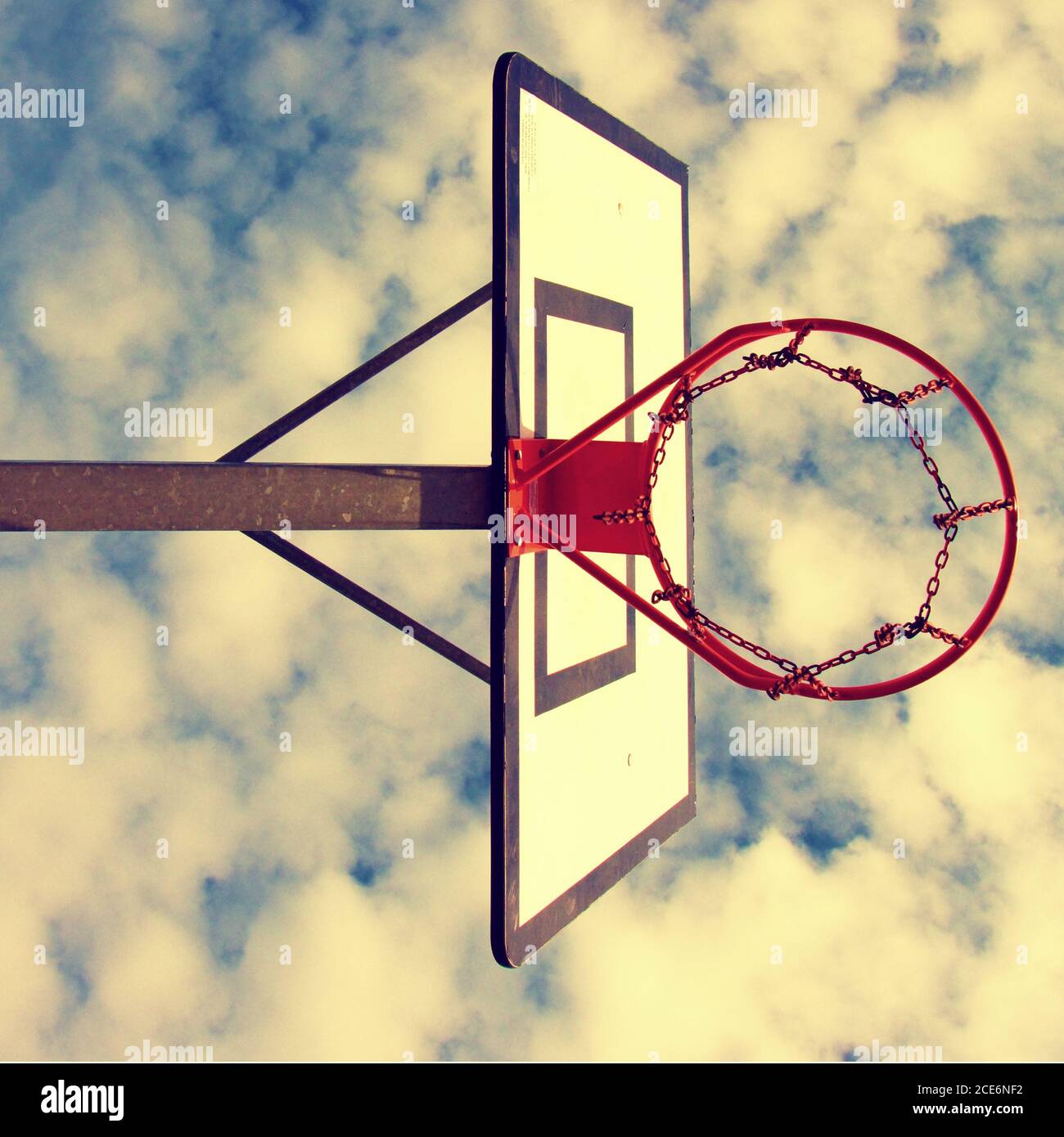 Vecchia negligenza basketball backboard con rusty hoop sopra il campo di strada. Cielo blu nuvoloso in terra di ckground. Filtro retrò Foto Stock