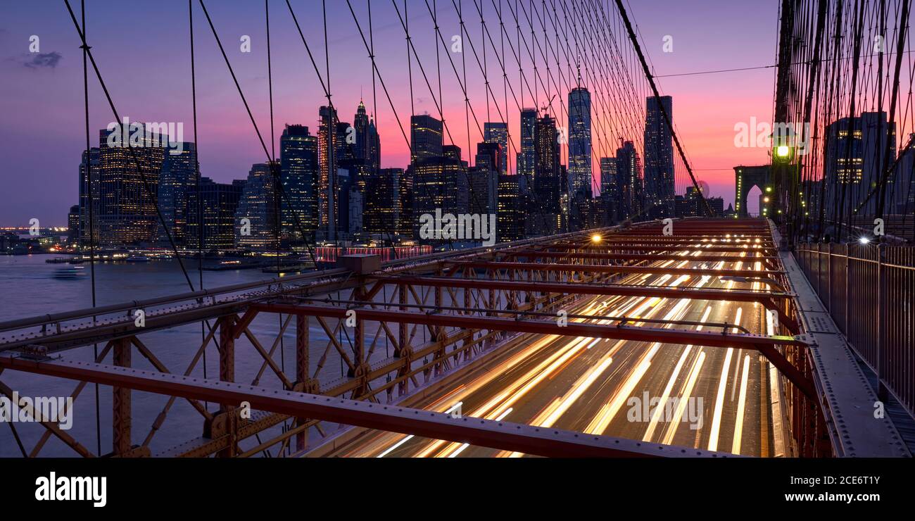 Ponte di Brooklyn con sentieri illuminati e vista sui grattacieli di Lower Manhattan al tramonto. Serata a New York City, NY, USA Foto Stock