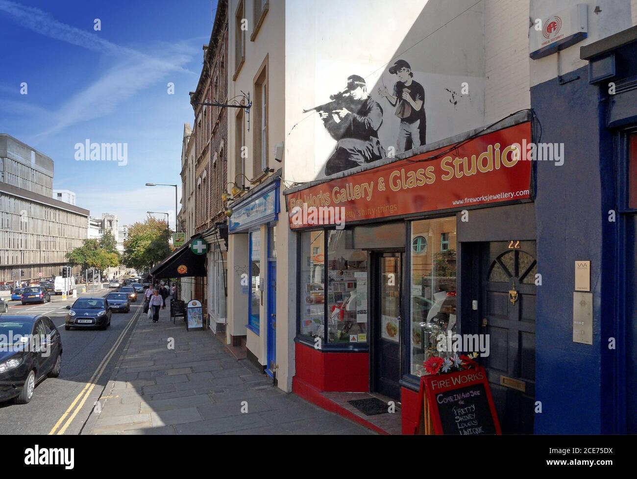 Banksy opere d'arte in Upper Maudlin Street a Bristol di un poliziotto armato accovacciato, con un bambino che sta per scoppiare una borsa di carta dietro di lui (ora andato) Foto Stock