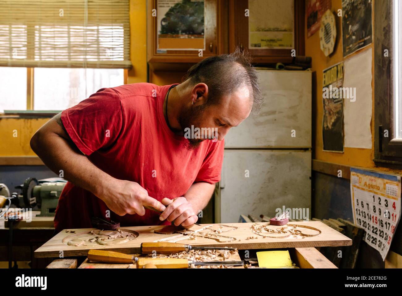 Intagliatore di legno usando scalpello di metallo mentre creando gli ornamenti su tavola lavori in officina Foto Stock