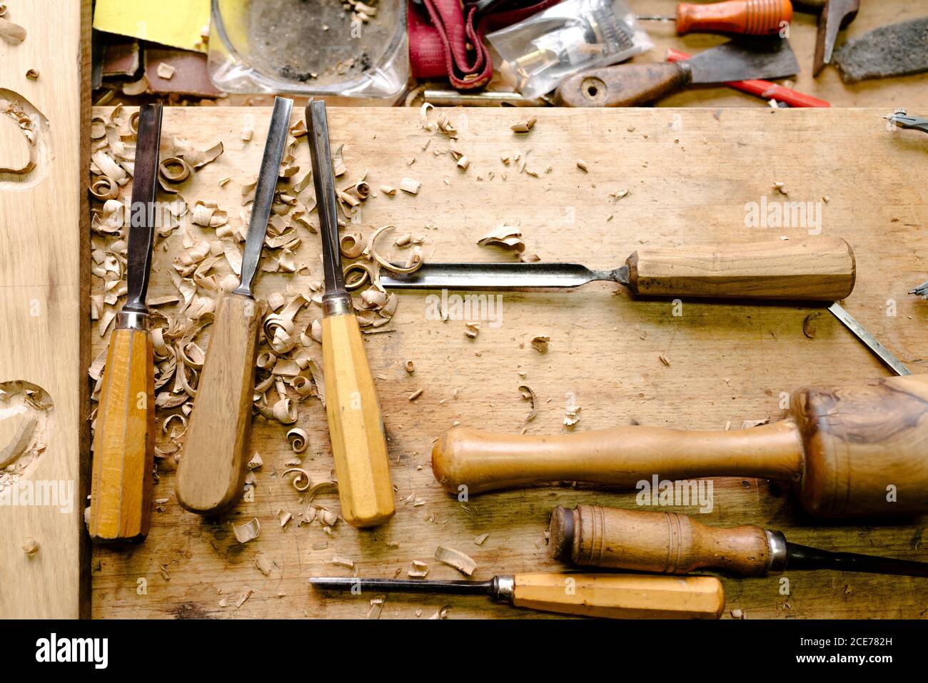Vista dall'alto del set di vari scalpelli per la scultura in legno posto su banco da lavoro disordinato con trucioli di legno Foto Stock