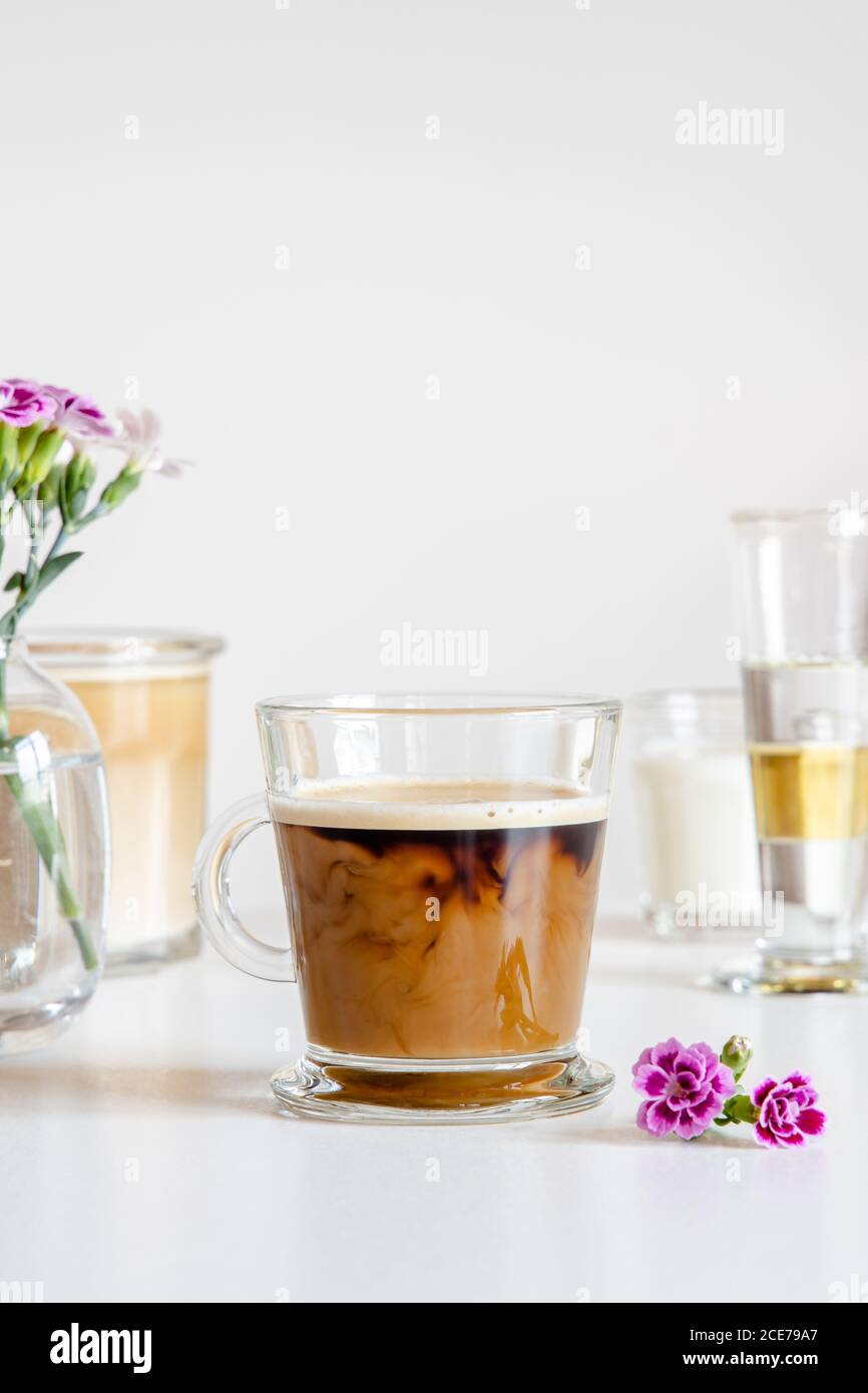 Caffè fresco aromatico ghiacciato con latte servito in tazza di vetro su tavolo decorato con fiori Foto Stock