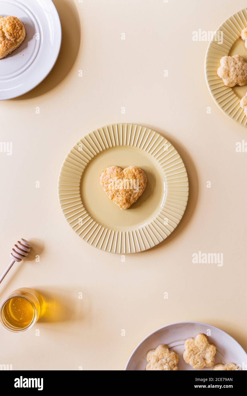 Vista dall'alto di deliziosi scones fatti in casa a forma di cuore e fiori serviti con miele naturale aromatico Foto Stock