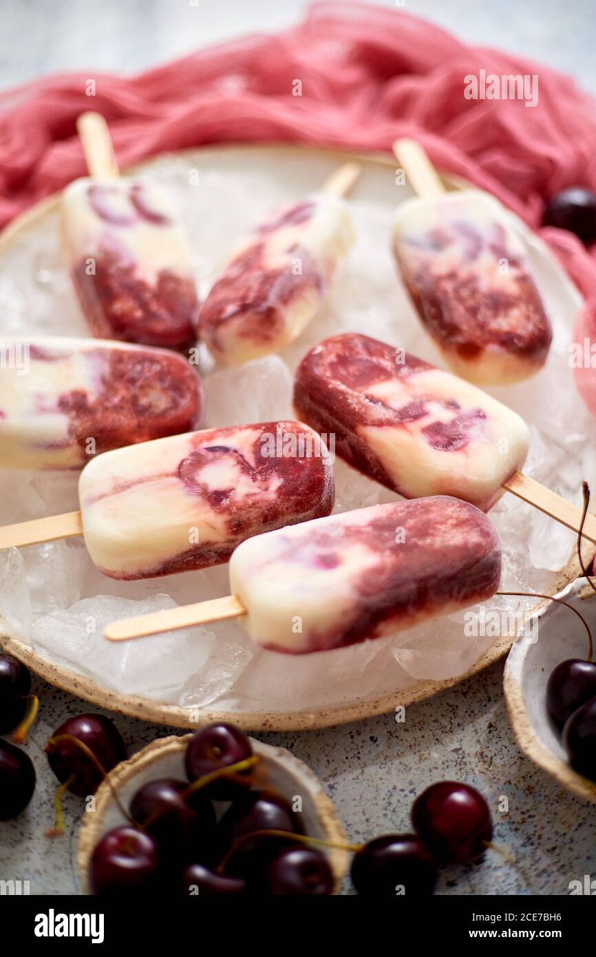 Panna fresca e ciliegia pop-icles fatti in casa posto su piastra di ceramica bianca con frutta e tessuto Foto Stock