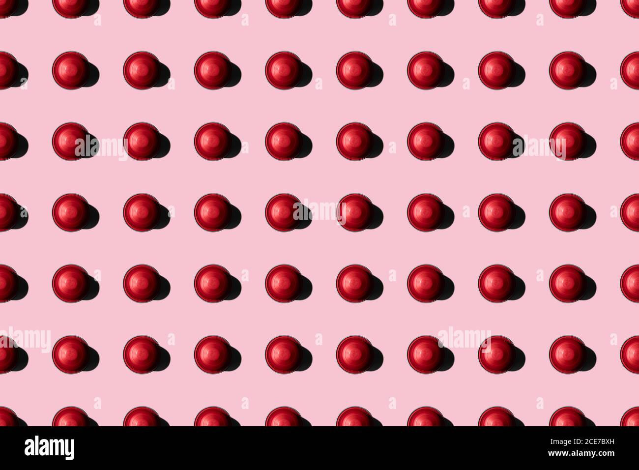 Vista dall'alto delle cialde di caffè rosse disposte in file uniformi come motivo senza cuciture su sfondo rosa Foto Stock