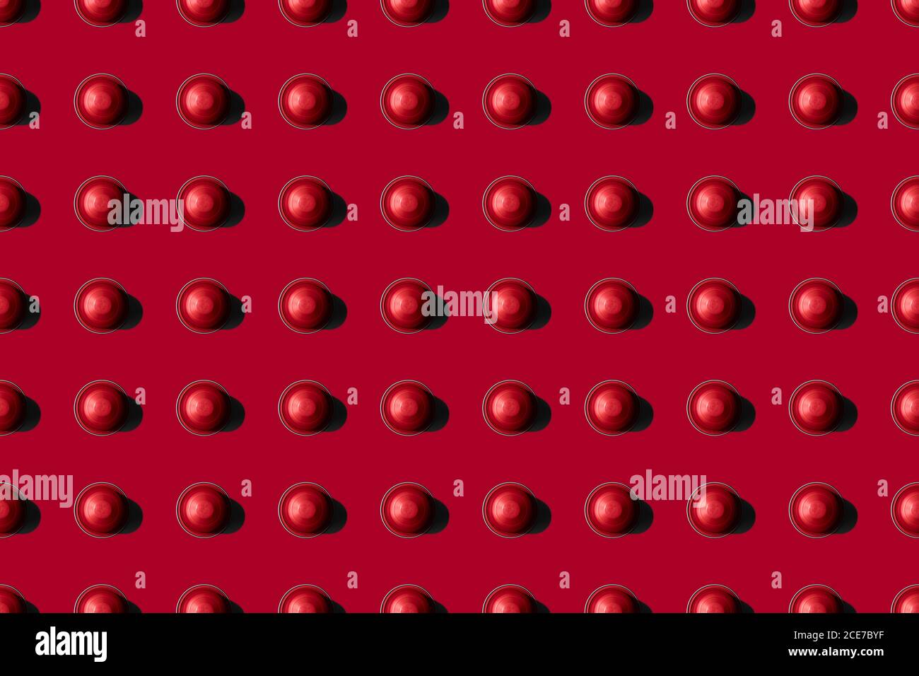 Vista dall'alto delle cialde di caffè rosse disposte in file uniformi come motivo senza giunture su sfondo rosso Foto Stock