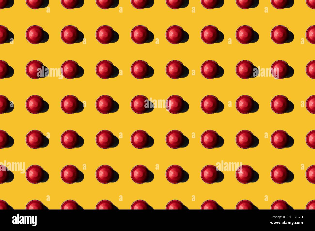 Vista dall'alto delle cialde di caffè rosse disposte in file uniformi come motivo senza giunture su sfondo giallo Foto Stock