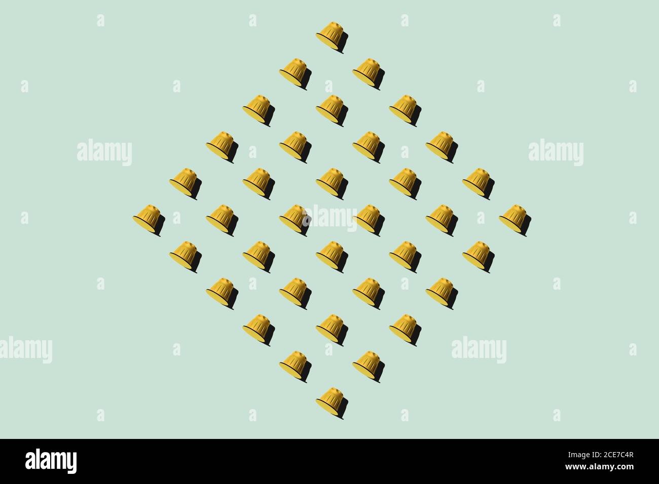 Vista dall'alto delle cialde di caffè gialle disposte in file uniformi come motivo senza giunture su sfondo verde Foto Stock