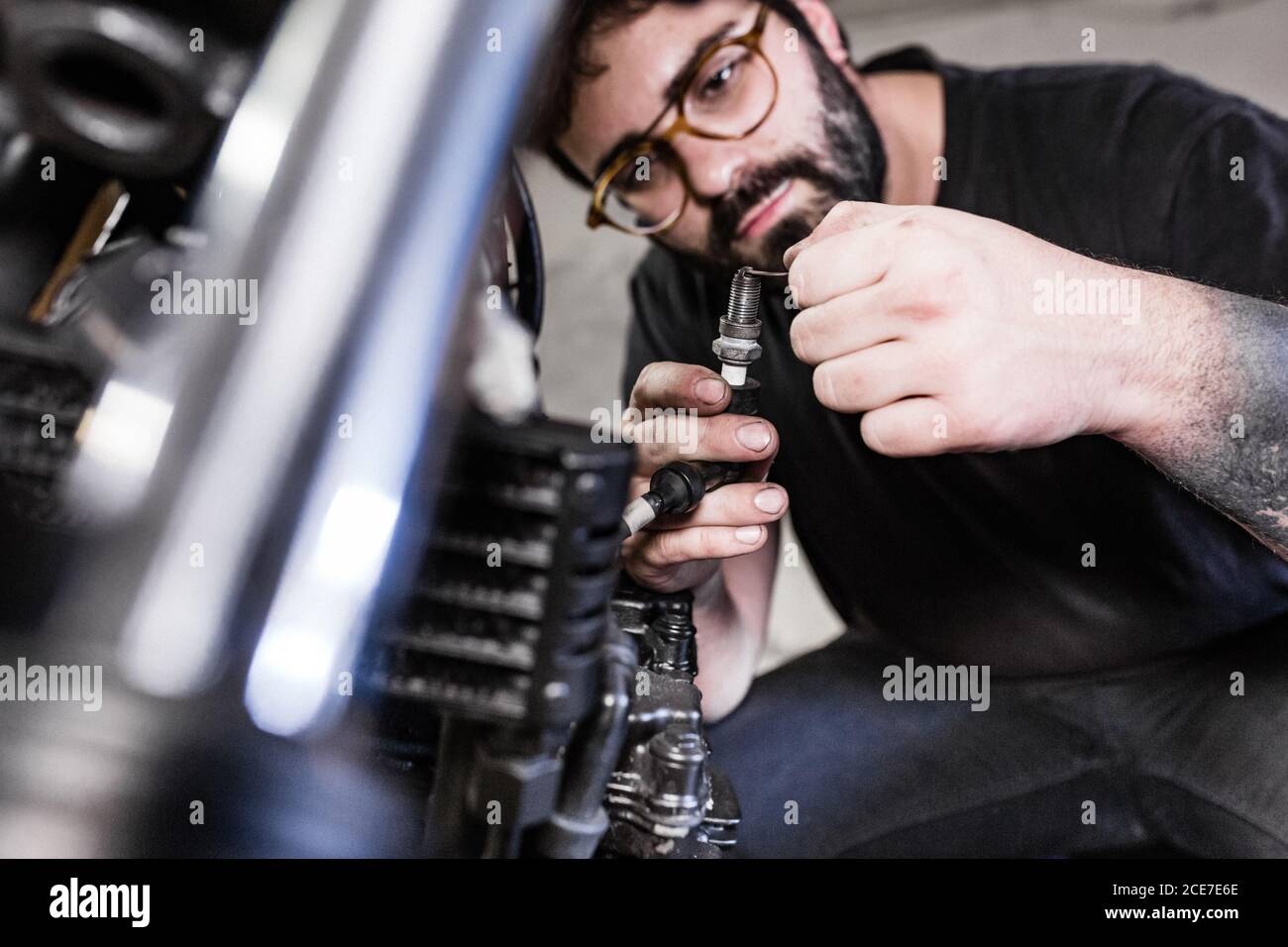 Meccanico maschio serio che ripara la candela sporca della moto mentre lavoro in garage Foto Stock