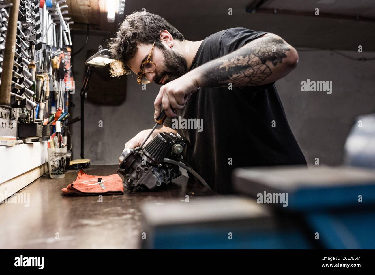 Vista laterale del brutale maestro maschile in piedi sul banco di lavoro e. dettaglio di riparazione del veicolo Foto Stock