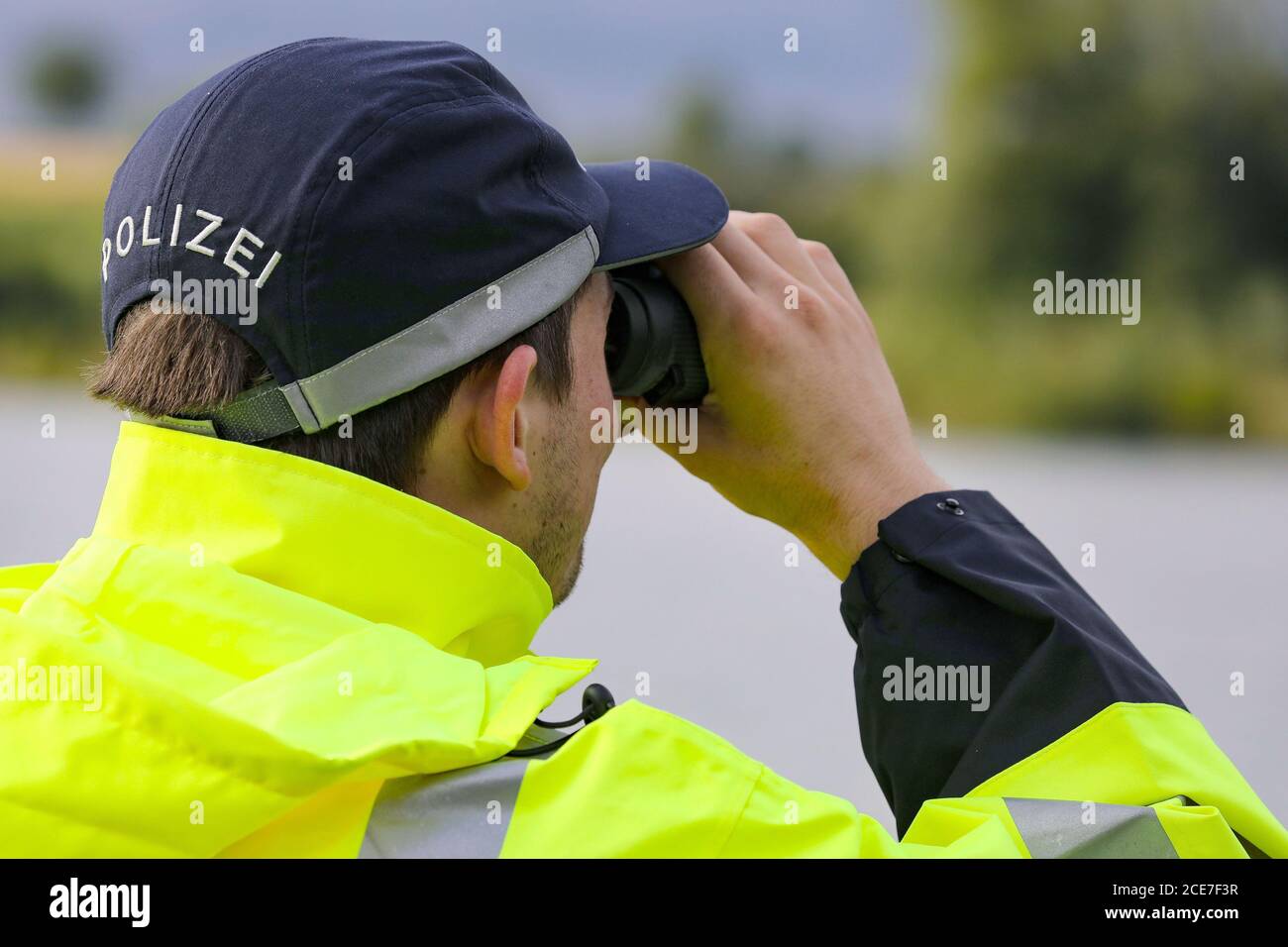 Dresda, Germania. 28 Agosto 2020. Un ufficiale di polizia in un impermeabile giallo-verde con l'iscrizione polizia sulla schiena sta guardando un corpo d'acqua con binocolo. Credit: Tino Plunert/dpa-Zentralbild/ZB/dpa/Alamy Live News Foto Stock