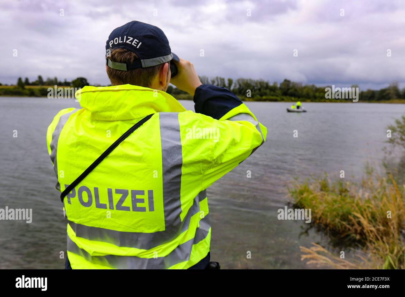 Dresda, Germania. 28 Agosto 2020. Un ufficiale di polizia in un impermeabile giallo-verde con l'iscrizione polizia sulla schiena sta guardando un corpo d'acqua con binocolo. Credit: Tino Plunert/dpa-Zentralbild/ZB/dpa/Alamy Live News Foto Stock