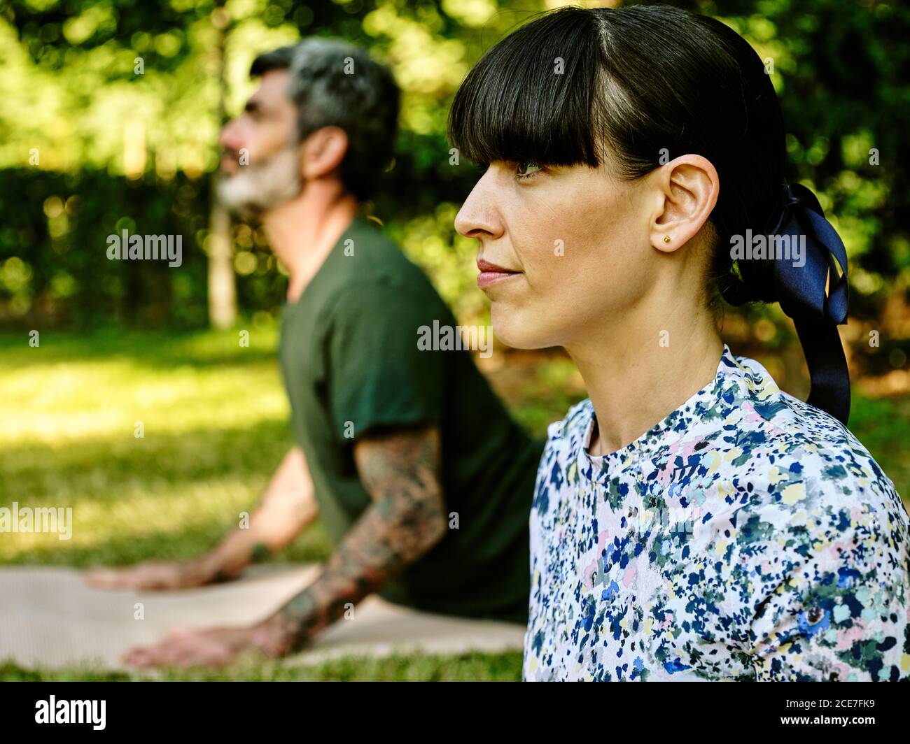 Vista laterale di una coppia serena che pratica yoga a Bhujangasana ON tappetini nel parco verde d'estate Foto Stock