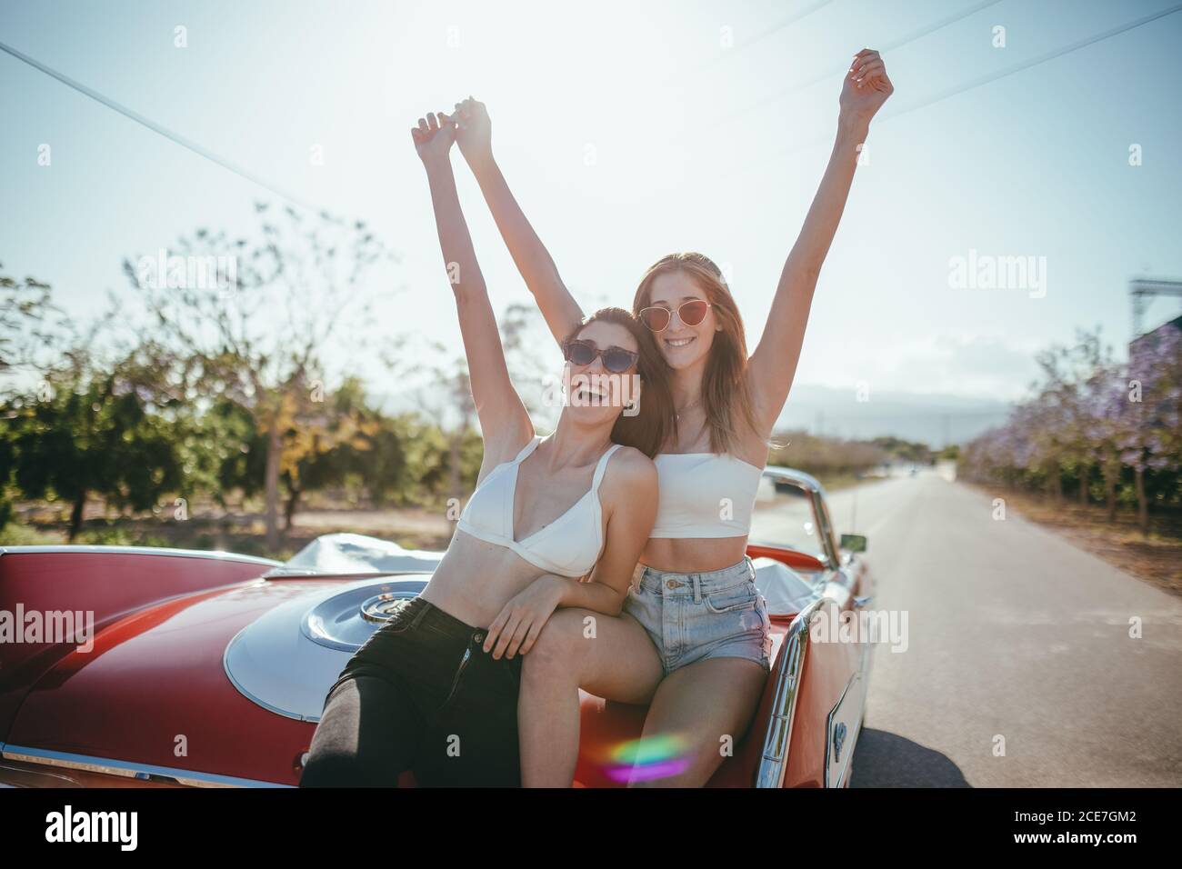 Allegre amiche d'estate indossano appoggiandosi al cabriolet e. godendo la vacanza con le braccia sollevate Foto Stock
